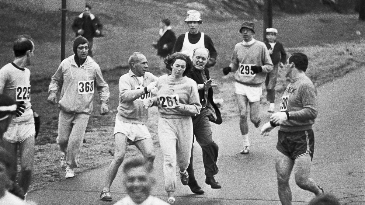 Η Kathrine Switzer, η πρώτη γυναίκα που επισήμως έτρεξε στον Μαραθώνιο της Βοστόνης. Στην φωτογραφία, παρενοχλείται από άντρα της διοργάνωσης που επιθυμεί να παραμείνουν οι αθλητικοί αγώνες, αντρική υπόθεση. Ηνωμένες Πολιτείες, 1967.
Ο σύντροφος της Kathrine Switzer και άλλοι δρομείς, έδιωξαν τον άντρα και την προστάτευσαν φτιάχνοντας μία ανθρώπινη ασπίδα γύρω της για τον υπόλοιπο αγώνα.